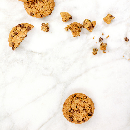 Chocolate chips cookies and crumbs, shot from above on a white marble background, with a place for text, square photo