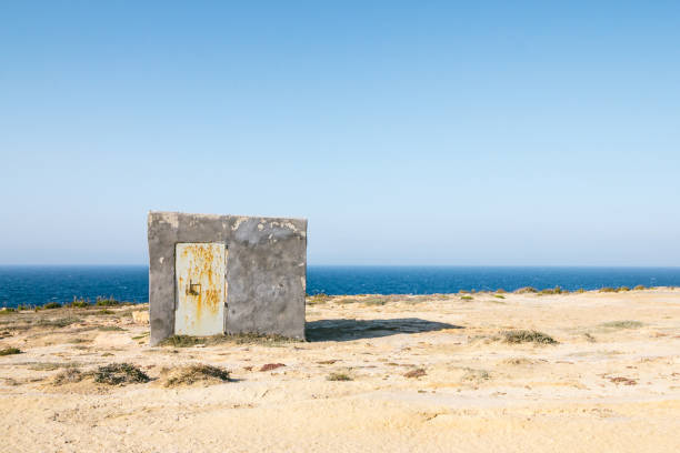 Illegally constructed concrete shelter on limestone cliffs in Gozo, Malta close to wied il-mielah. Barren landscape with the sea and blue sky. stock photo