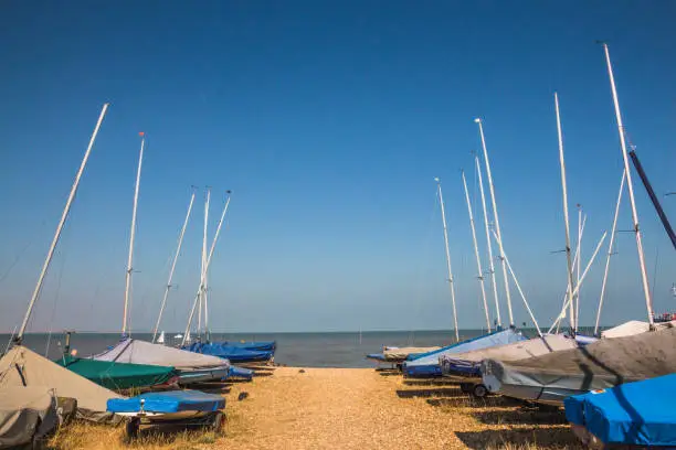 Photo of Small sailing boats lined up near the sea on the sand at Whitstable, Kent, United kingdom