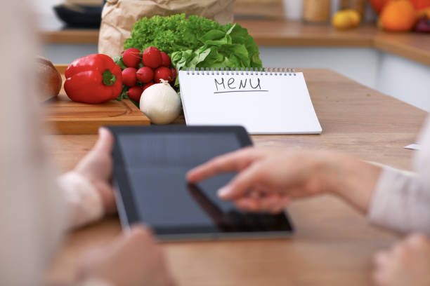 istock Human hands of two female persons using touchpad for making menu in the kitchen. Closeup of two women are making online shopping by tablet computer and credit card. Cooking and shopping concept. 682727576