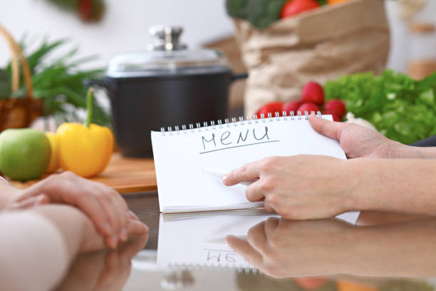 istock Human hands pointing into note book with copy space area. Two woman making menu in the kitchen, closeup. Cooking and friendship concept. 682728164