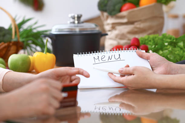 istock Human hands pointing into note book with copy space area. Two woman making menu in the kitchen, closeup. Cooking and friendship concept. 682728212