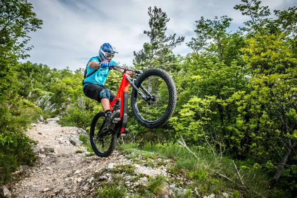 Enduro All Mountain Electric bicycle rider - adrenaline rock MTB trail: A panoramic hill Sabotin above Nova Gorica, where Dinarides collide with the Alps and next to which Soča River exits its narrow valley and leaves Slovenia - entering to Italy. Blurred motion. All logos removed or covered. Nikon, outdoor photography.