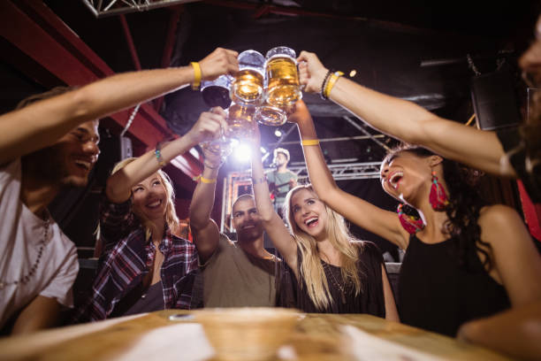 Low angle view of happy friends toasting beer glasses while sitting at table in club