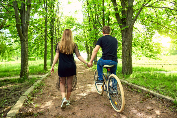 istock A loving couple on  bicycle holds hands in  park. Back view 682735942