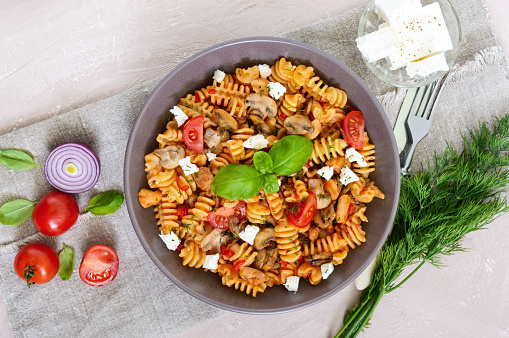 Pasta Radiatori with chicken, mushrooms, cherry tomatoes, feta cheese and tomato sauce on a light background. Top view.