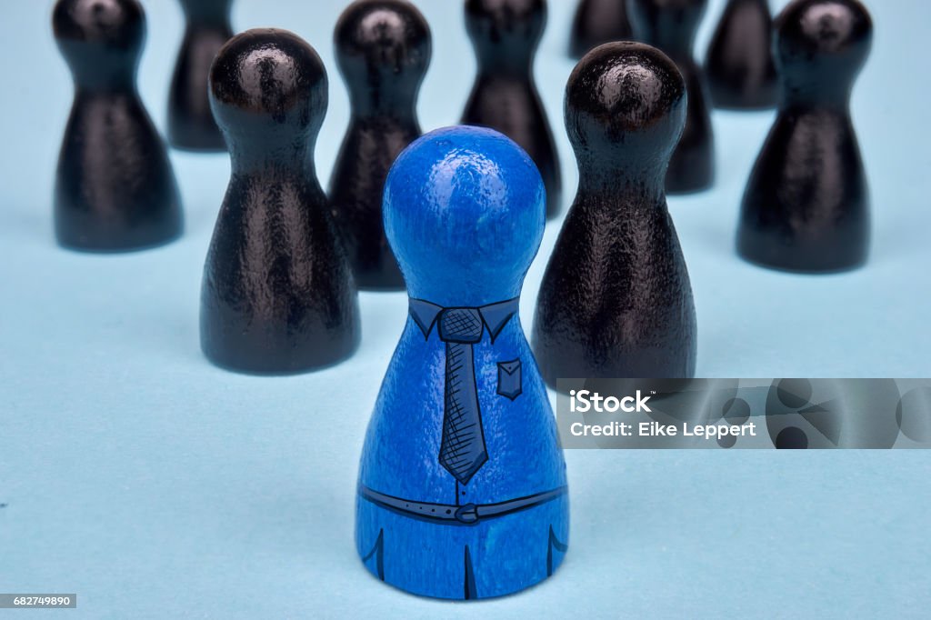 Teamleader with his team. Symbol for leadership with game figures in blue and black and drawn suit elements. Boss or leader stands in the middle with a drawn suit. Chief - Leader Stock Photo