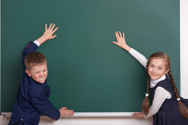 istock elementary school boy and girl put hands on chalkboard background and show blank space, dressed in classic black suit, group pupil, education concept 682752196