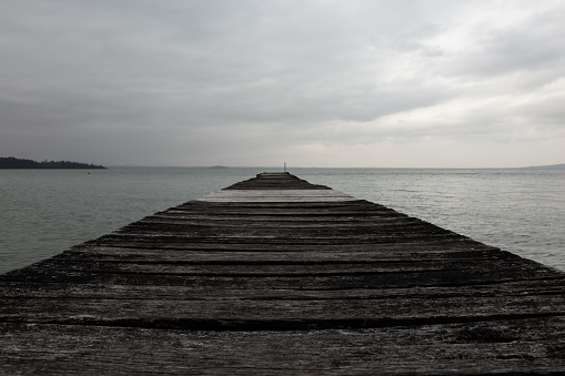 A very low, first person view of a pier on a lake, with cloudy sky
