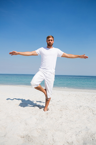 Man exercising on sand at beach against clear blue sky