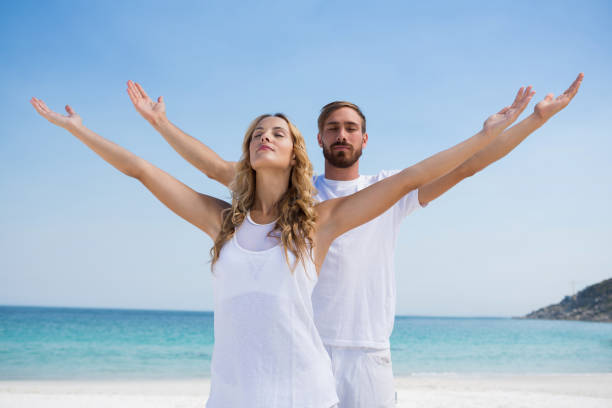 Couple with arms outstretched exercising while standing at beach