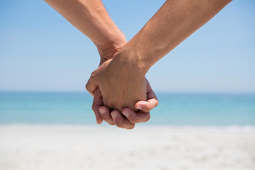 Cropped hands of couple holding hands at beach