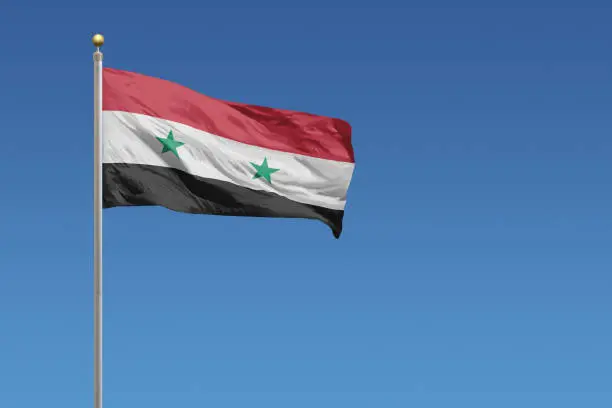 Flag of Syria in front of a clear blue sky