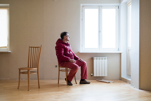 Mature caucasian white man, 45 years old, sitting on the chair in the empty living room. Minsk, Belarus, Eastern Europe