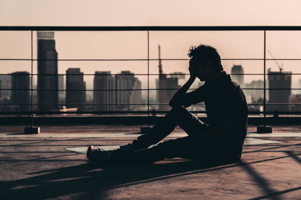 Silhouette of sad depressed Asian man lost hope and cry, sit on building rooftop at sunset, dark mood tone. Concept of major depressive disorder, friend zone, unemployment, stress emotion or paranoid Silhouette of sad depressed Asian man lost hope and cry, sit on building rooftop at sunset, dark mood tone. Concept of major depressive disorder, friend zone, unemployment, stress emotion or paranoid suicide photos stock pictures, royalty-free photos & images