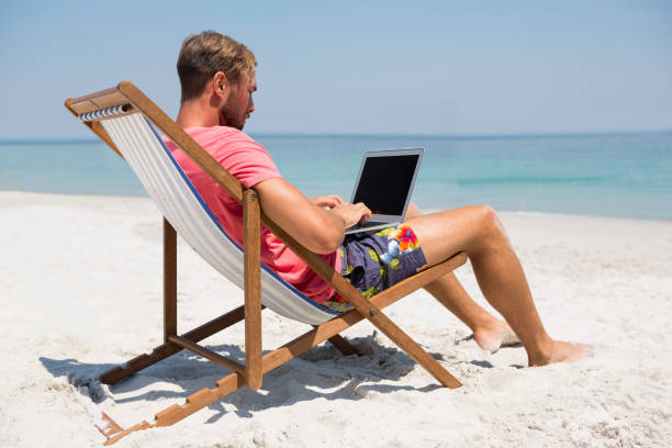 istock Full length of man using laptop at beach 682828754