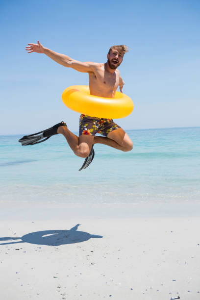 istock Playful man wearing inflatable ring jumping on shore 682829354