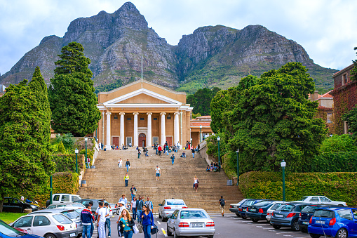 Cape Town, South Africa - April 17, 2007: The main building in the University of Cape Town in South Africa, with the Devil's Peak in the background. Photo shot in the afternoon sunlight; horizontal format. Several cars are parked in front of the steps to the building. Many students can be seen walking away or to the building; some just sit on the steps relaxing or chatting with friends. Image shot in the afternoon sunlight. Horizontal format.