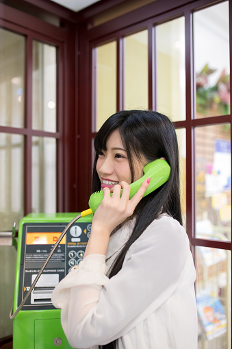 Happy young woman talking over the phone in telephone box