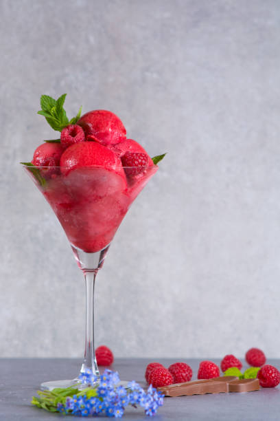 istock Raspberry ice cream sorbet in glass with chocolate spoon, raspberry, mint leaves and blue flowers, copy space 682876604