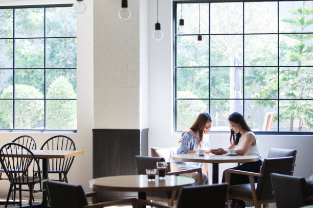 In the bright sunshine, two college girls spend in a beautiful restaurant. Two college girls spend at restaurants with big windows. restaurant window stock pictures, royalty-free photos & images