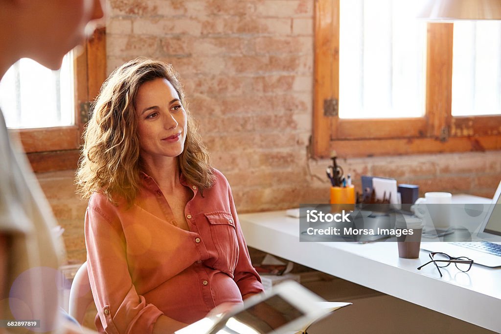 Pregnant businesswoman looking away at desk - Foto de stock de Mulheres royalty-free