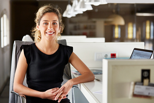 Portrait of confident businesswoman sitting at desk. Young female executive is smiling. She is wearing dress in office.