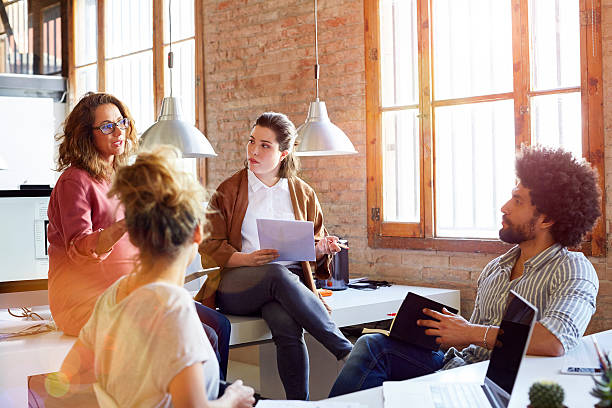 Pregnant businesswoman discussing with colleagues Pregnant businesswoman communicating with colleagues. Male and female executives are sitting in office. Creative business people are sharing ideas. leanincollection stock pictures, royalty-free photos & images