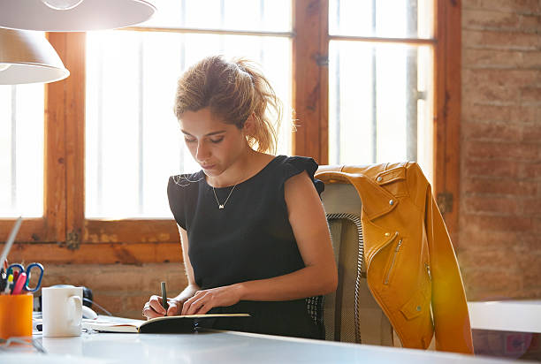 businesswoman writing in book at desk - women black lighting equipment business 뉴스 사진 이미지