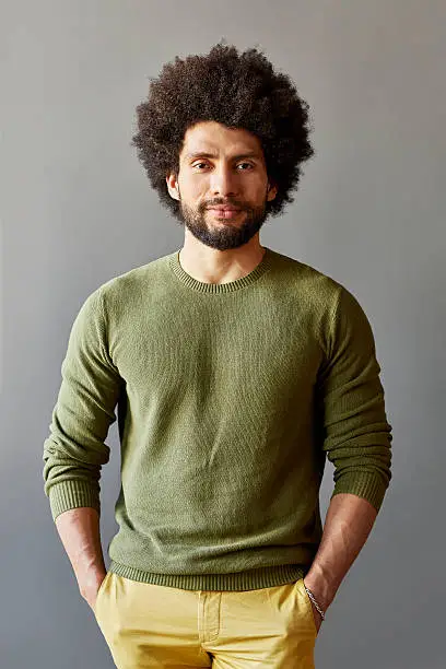 Portrait of confident businessman with hands in pockets. Smart male professional is wearing casuals. He is standing over gray background.