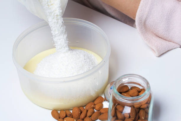 istock Walnut almonds. In a glass jar, scattered on the table. Next to the container with condensed milk into which a woman is pouring coconut shavings. On a white background. 682901294