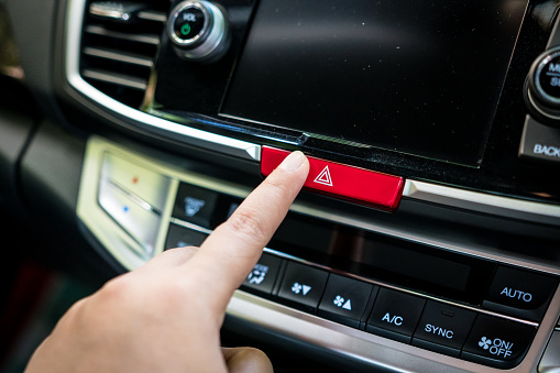 finger pressing the car emergency button on car's dashboard, inside car.