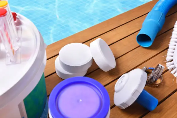 Chemical products and tools for the maintenance of the pool on wooden slats. Pool with water and blue mosaics background. Horizontal composition. Top elevated view.