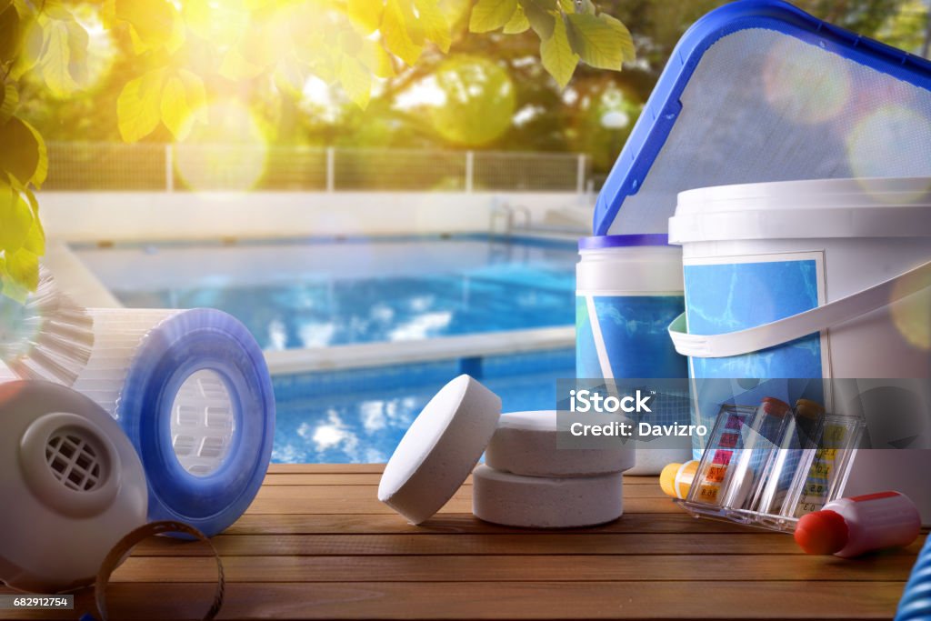 Swimming pool service and equipment with swimming pool background Swimming pool service and equipment with chemical cleaning products and tools on wood table and pool background. Horizontal composition. Front view Swimming Pool Stock Photo