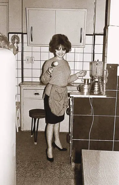 Vintage black and white photo from the sixties featuring a young woman cooking in the kitchen