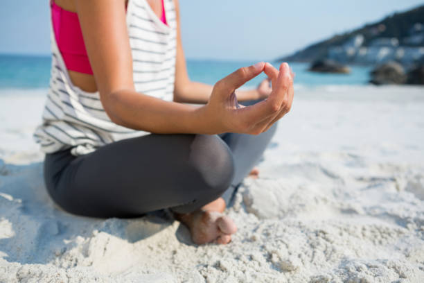 istock Low section of woman meditating while sitting on sand at beach 682937096