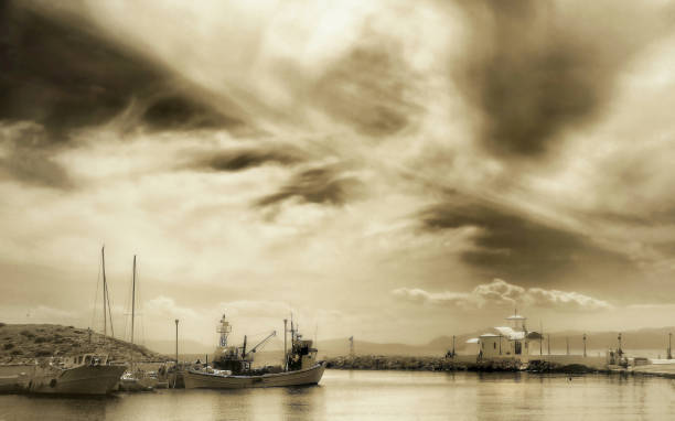 marino griego con una pequeña capilla y barcos de pesca bajo un cielo espectacular en puerto .sepia tono editado - retro fish day sunset sunlight fotografías e imágenes de stock