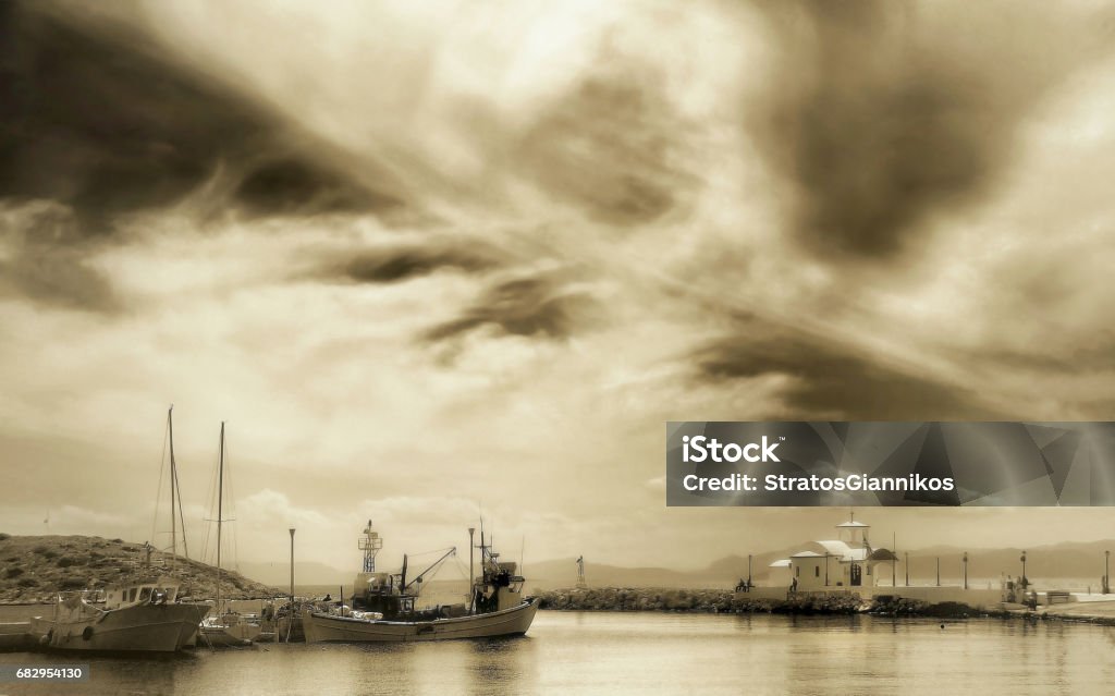 Greek seascape with a small chapel and fishing boats under a dramatic sky in harbour .sepia tone edited Cloud - Sky Stock Photo