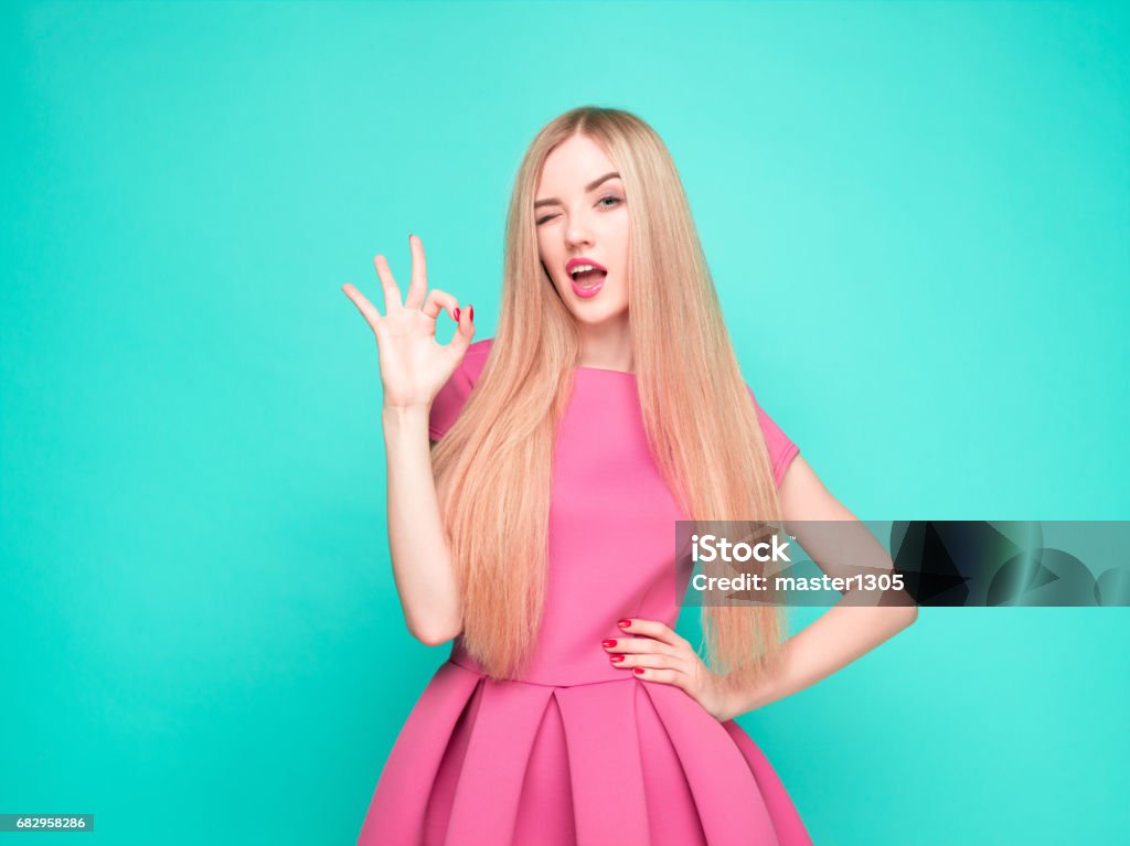 The beautiful young woman in pink mini dress posing at studio The beautiful young woman in pink mini dress posing at the studio on blue background. Dress Stock Photo