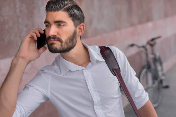 I'm early anyway people, style, leisure and lifestyle - young hipster man with  shoulder bag, fixed gear bike on city street over wall background during the day using his smartphone  in his way to work. anyway stock pictures, royalty-free photos & images