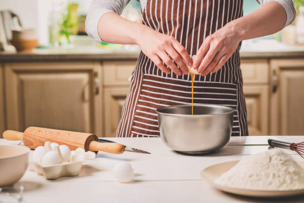 istock Young woman breaking egg over bowl with dough, close-up 683035726