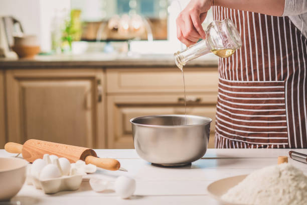 istock Young woman pouring oil into a bowl with dough, close-up 683035766