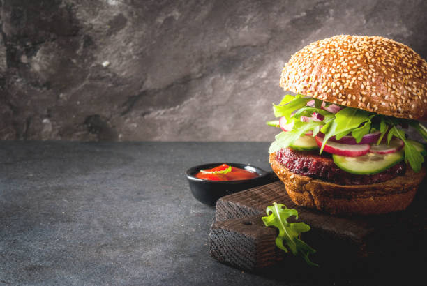 Healthy vegan burgers Healthy vegan burgers with beets, carrots, spinach, arugula, cucumber, radish and tomato sauce, whole grain buns on a rustic wooden board on a dark stone background, selective focus, copy space veggie burger photos stock pictures, royalty-free photos & images
