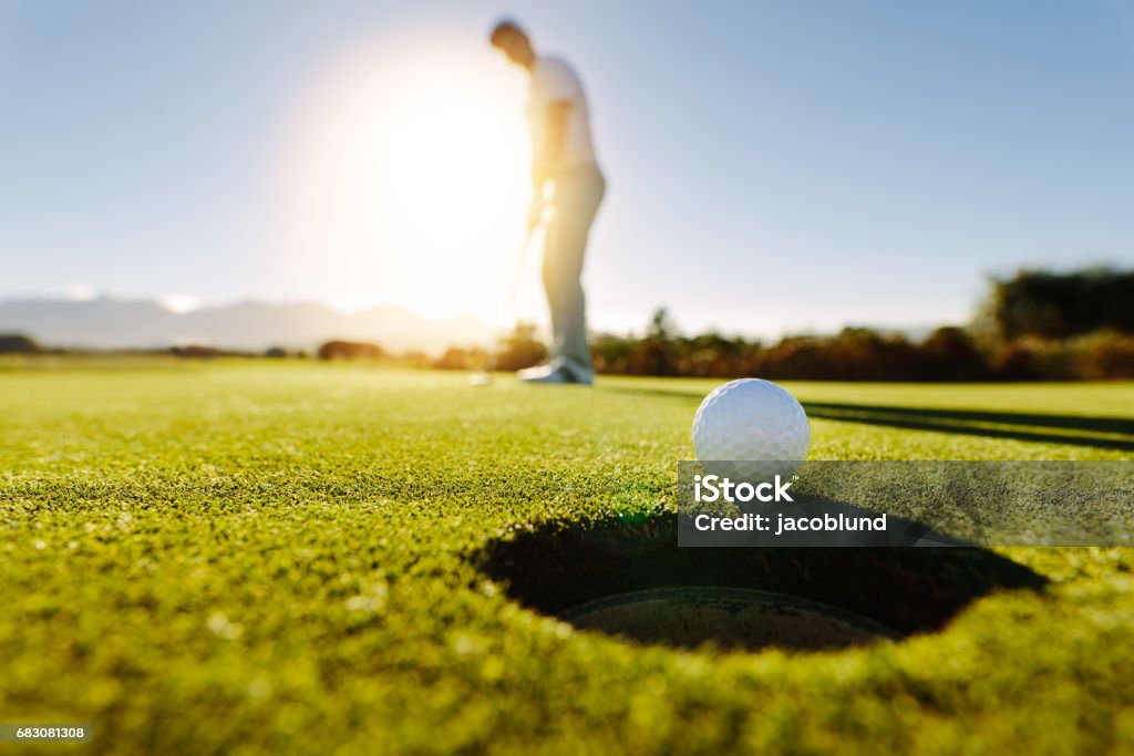 Man puts the ball on golf course green Pro golfer putting golf ball in to the hole. Golf ball by the hole with player in background on a sunny day. Golf Stock Photo