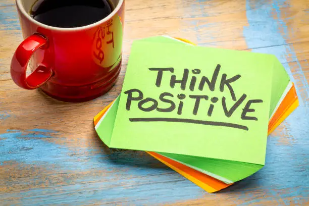 think positive - inspirational handwriting in a green sticky note with a cup of coffee