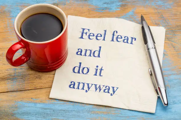 Feel fear and do it anyway - motivational handwriting on a napkin with a cup of coffee