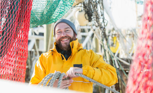 Man working on commercial fishing vessel A mature man wearing a raincoat, working on a commercial fishing vessel, a shrimp boat. Fishing nets are hanging down around him. fisherman photos stock pictures, royalty-free photos & images