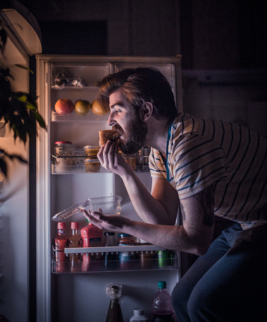 Young handsome man eating late night in front of the refrigerator