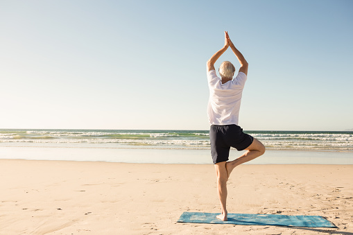 Rear view of senior man practicing tree pose at beach on sunny day