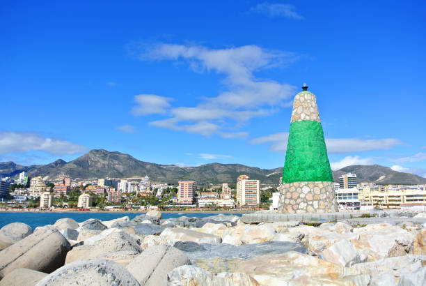 A view to Mediterranean sea, a lighthouse with breakwaters and hotels at the background from a pier at Benalmadena port Puerto Marina, Andalusia, Spain.